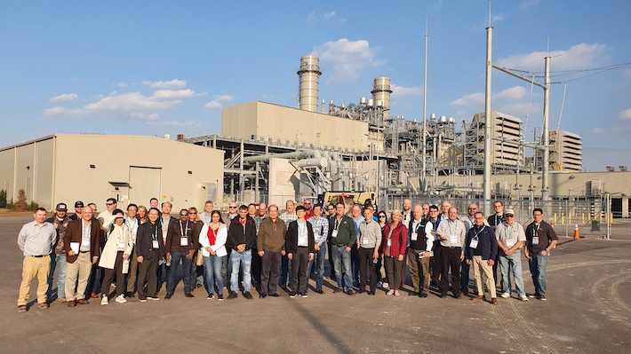 Large tour group standing in front of a power-generation plant