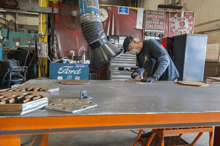A man wearing a safety mask grinds metal in front of an air duct